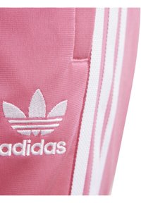 Pink polyester fabric featuring a white embroidered Adidas logo and three white stripes along the side. Smooth texture with durable stitching.