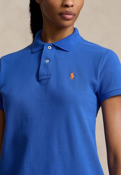 Blå polo skjorte laget av teksturert stoff med tre-knapp placket, kort erm og en oransje brodert logo på brystet.