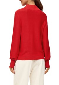 Roter Strickpullover mit einem hohen Kragen und gerippten Bündchen. Glatte Textur und lockere Passform, kombiniert mit cremefarbene strukturierten Hosen.