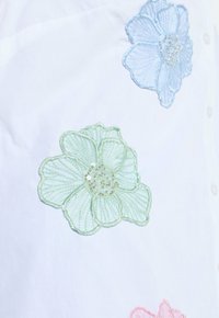 White fabric with embroidered pastel flowers in blue, green, and pink, each detailed with beads in the center.