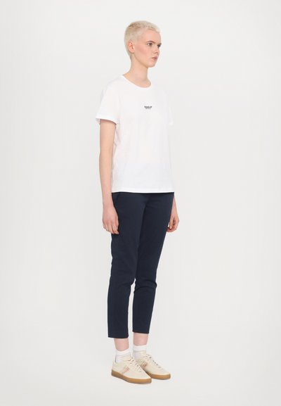 Hvid bomulds T-shirt med rund hals og korte ærmer, parret med mørkeblå slim-fit bukser og lyse sneakers med røde accenter.