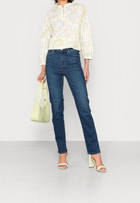 Blouse à motif floral clair avec col, jeans en denim bleu, sandales à talons blocs blanches et sac à main vert clair.