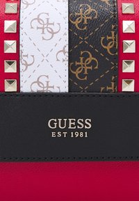 Rotes, weißes und schwarzes Leder mit goldenen Nieten, gemusterten Riemen und "GUESS EST 1981" in gold auf schwarzem Leder geprägt.