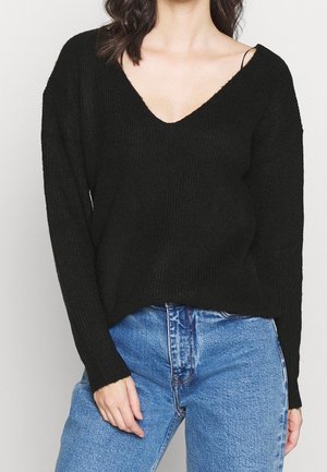 Maglione nèro a coste con scollatura a V profonda e maniche lunghe, abbinato a jeans di denim blu chiaro. Il maglione ha una vestibilità comoda e una texture morbida.