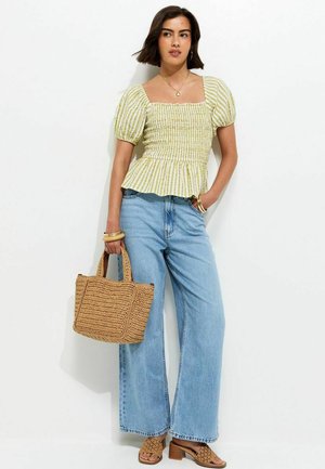 Femme portant un haut rayé à manches ballon, un jean bleu à jambes larges, tenant un sac à main tressé beige, et portant des sandales tressées à talons blocs assorties.
