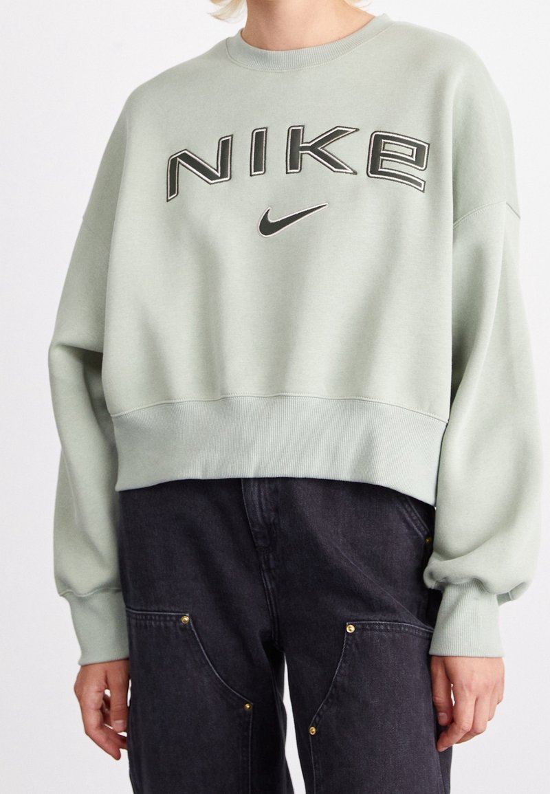 Ljust grön kortärmad sweatshirt med "NIKE"-logotyp, ribbade muddar och hals. Kombinerad med mörka denimbyxor med fickdetaljer.