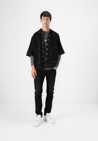 Black short-sleeve shirt with contrasting stitching, layered over a gray t-shirt, paired with black jeans and white sneakers.