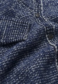 Marineblauwe cardigan met een textuurgebreid patroon en contrasterende witte draden. Heeft een knoopsluiting en een borstzak.
