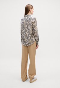 Blusa de manga longa com um padrão paisley em bege e azul marinho, combinada com calças largas de um tom claro de bege e ténis creme. Textura do tecido suave.