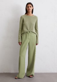 Lichtgroene gebreide trui met een ronde hals, gecombineerd met wijde lichtgroene broek met een elastische taille en zijzakken.