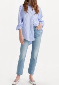 Randig blå och vit skjorta med knappar och uppvikta ärmar, tillsammans med bleka ljusblå raka jeans och silvriga flats.