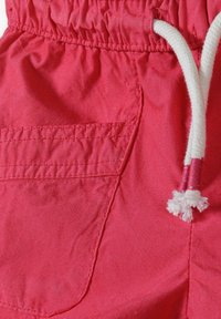 Primo piano di pantaloni corti rossi con tasca laterale, vita elasticizzata e cordoncino bianco con punte rosse.