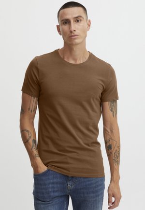 Braunes Kurzarm-T-Shirt in taillierter Form, gefertigt aus glattem Baumwollstoff, kombiniert mit blauen Denim-Jeans. Lässiger Look mit sichtbaren Arm-Tattoos.