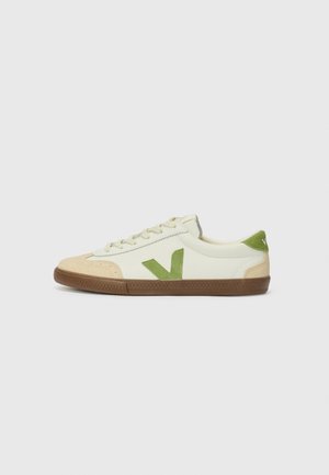 Sneakers bianchi con dettagli verdi e punta in suede beige. Presentano una suola in gomma testurizzata e un design con lacci. Stile minimalista.