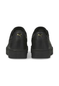 Czarne skórzane sneakersy o gładkiej teksturze, z niskim krojem i złotymi akcentami logo Puma na pięcie. Gruba gumowa podeszwa.