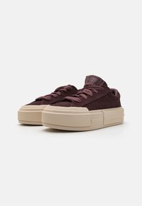 Baskets en daim bordeaux avec semelles en caoutchouc beige, présentant des lacets ronds et un col rembourré. Bout carré et motif texturé sur la semelle.