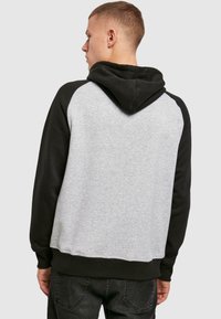 Schwarzer und grauer Kapuzenpullover mit Kängurutaschen, gerippten Bündchen und Saum. Verfügt über einen grauen Körper und schwarze Raglanärmel mit einer verstellbaren Kapuze.