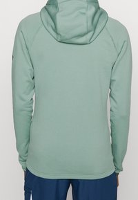 Sweat à capuche en tissu doux vert menthe. Comprend des manches longues, une coupe ajustée et une texture lisse sans motifs ni accents visibles.