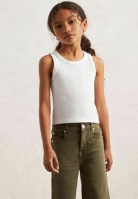 Weißes, geripptes Tanktop, kombiniert mit olivgrünen, weit geschnittenen Hosen mit Fronttaschen und Metallakzenten.