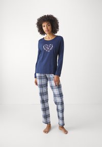 Mörkblå långärmad pyjamatopp med blommig hjärt-grafik; rutiga byxor i blått, vitt och svart. Mjuk bomullsblandning, avslappnad passform.