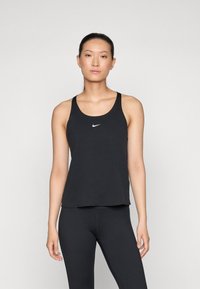 Černý sportovní top bez rukávů se širokými ramínky a kulatým výstřihem. Na hrudi je malé bílé logo Nike. Hladká tkanina, volnější střih.