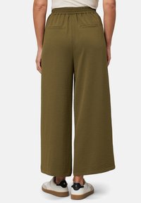 Wide-leg, olive green pants in a textured fabric with an elastic waistband and two back pockets. Worn with white sneakers.