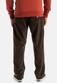 Brown corduroy pants with a relaxed fit, featuring back pockets and subtle ribbed texture. Paired with dark footwear.