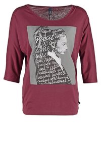 Burgundy t-shirt with three-quarter sleeves, featuring a gray graphic print of a profile and white text. Soft fabric, relaxed fit.
