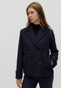 Marinblå dubbelknäppt ulljacka med slagkrage, knappprynkningar och två sidofickor. Mjuk, texturerad tyg med avslappnad passform.