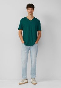 Turkusowa koszulka z dekoltem w serek, krótkie rękawy, zestawiona z jasnoniebieskimi dżinsami i beżowymi sneakersami. Prosty krój, miękka tekstura i luźny fason.