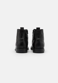 Botas de cuero negro hasta el tobillo con una textura suave, que cuentan con un cierre de cremallera, una lengüeta y un tacón bajo tipo bloque.