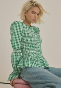 Grøn- og hvidternet bluse med puffede ærmer, smocket krop og peplum-kant, parret med lyseblå jeans.
