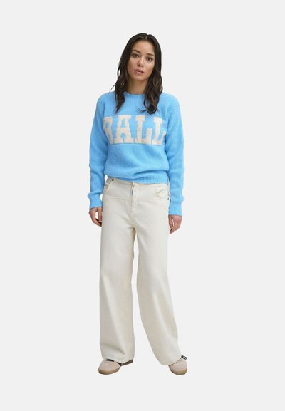 Lyseblå strikkegenser med "BALL" i kremfarge på forsiden, sammen med off-white vide jeans og beige slip-on sko.
