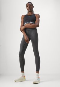Fekete sportmelltartó fehér szalaglogóval, magas derekú, testhez simuló fekete leggingszel párosítva. Fehér sportcipő színes részletekkel egészíti ki a megjelenést.