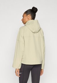 Ελαφρώς μπεζ μπουφάν με κουκούλα και άνετη εφαρμογή, φτιαγμένο από υφή υφάσματος. Διαθέτει χαμηλωμένους ώμους και απλό σχεδιασμό χωρίς ορατά μεταλλικά στοιχεία.