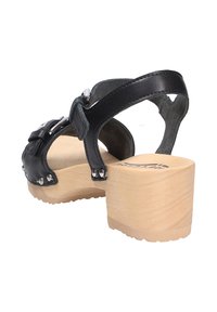 Schwarze Leder-Clog-Sandale mit verstellbarem Knöchelriemen, Holzplattformabsatz, silbernen Hardware-Akzenten und strukturiertem Profil.
