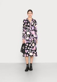 Vestido de manga longa com estampa floral em rosa, roxo e branco sobre um fundo preto, apresentando um decote de colarinho e uma silhueta fluida.