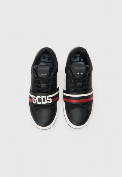 Zapatillas de cuero negro con suela blanca, con un prominente logo de GCDS y franjas de acento rojas y blancas en la parte superior.