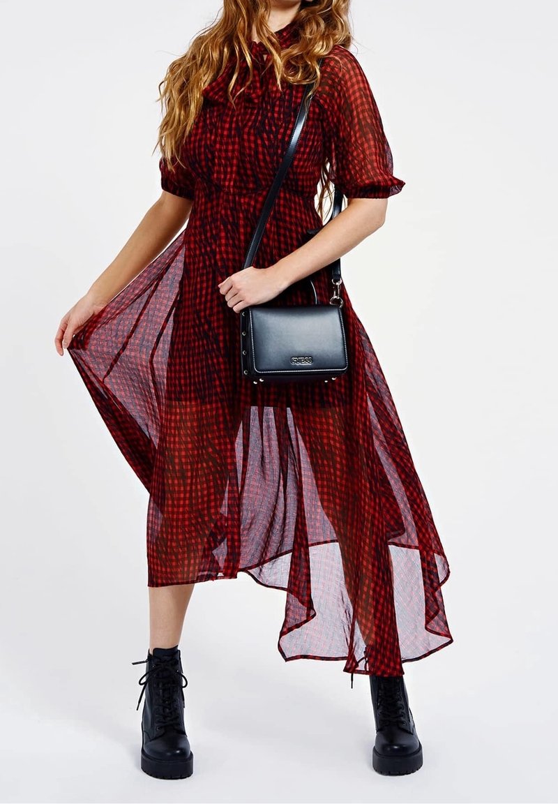 Röd och svart rutig genomskinlig klänning med korta ärmar, hög-låg fåll, som är kombinerad med en kompakt svart handväska och kraftiga svarta stövlar.