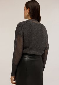 Grau gestrickter Pullover mit transparenten Ärmeln, strukturiertem Material, runder Ausschnitt, kombiniert mit einem schwarzen Lederrock, der die geschichteten Designs betont.