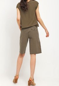Oliven Grønne shorts lavet af blødt bomuldsstof med en afslappet pasform, knælang, med baglommer og et fladt frontdesign.