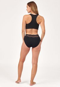 Soutien-gorge de sport noir avec un design dos nageur, associé à des sous-vêtements noirs taille haute avec une taille en dentelle. Texture lisse, forme ajustée.