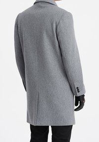 Šedý vlněný kabát s klasickým střihem, klopovým límcem a detaily tří knoflíků na manžetě. Látka má texturovaný vzhled.