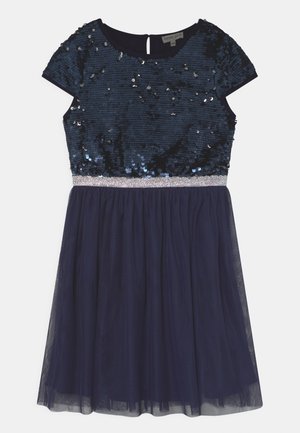 Vestido de marinero con un cuerpo de lentejuelas, mangas cortas y una falda de tul. Cuenta con una cintura plateada y un cierre de llave en la espalda.