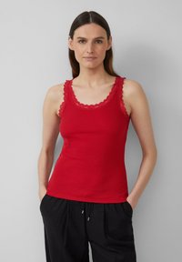 Rotes geripptes Tanktop mit gewelltem Spitzenrand entlang des Ausschnitts und der Armausschnitte, figurbetontes Design, kombiniert mit lockeren schwarzen Hosen.