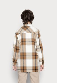 Checkered flannel shirt in beige, brown, and white. Features a classic collar, long sleeves, and button cuffs with a relaxed fit.
