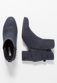 Botines de ante azul marino con tacón bloque, cremallera lateral y textura suave. Presenta una punta redondeada y un diseño minimalista.