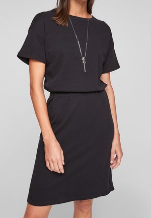 Robe t-shirt en coton noir avec des manches courtes, un col rond, une taille cintrée et un ourlet droit. Portée avec un long collier en argent.