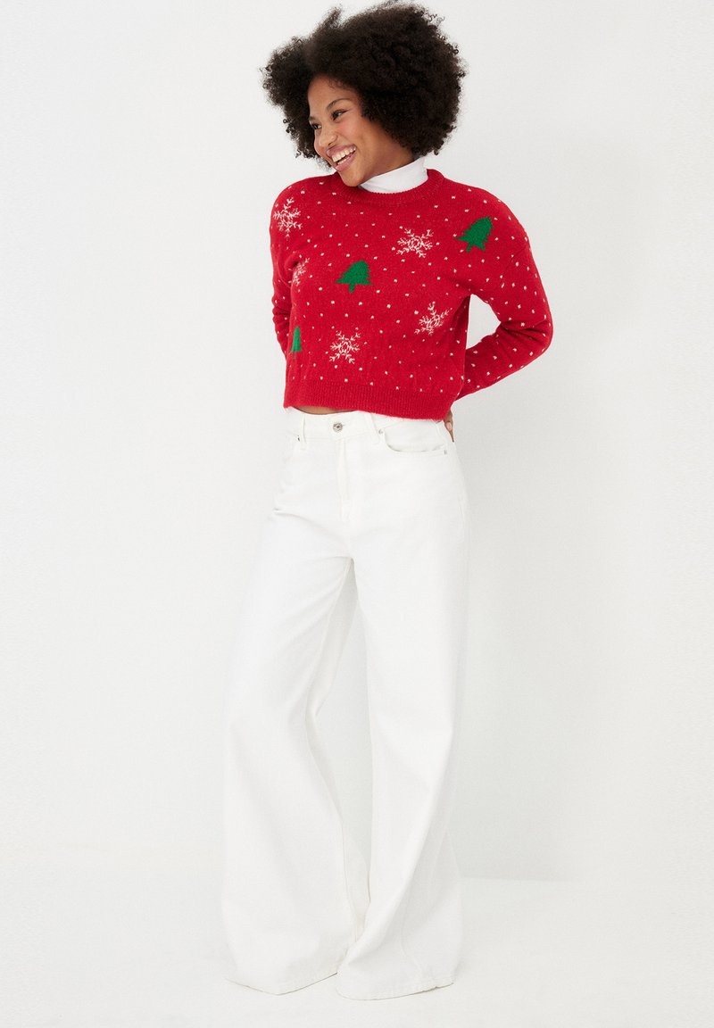 Czerwony wełniany sweter z zielonymi wzorami drzewka i śnieżynkami, w połączeniu z białymi spodniami z szerokimi nogawkami. Krótkie wykończenie, okrągły dekolt i długie rękawy.