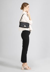 Borsa nera con dettagli a trapunta, hardware in argento e una tracolla. Indossata con una camicia beige chiaro e jeans neri aderenti, con tacchi chunky.
